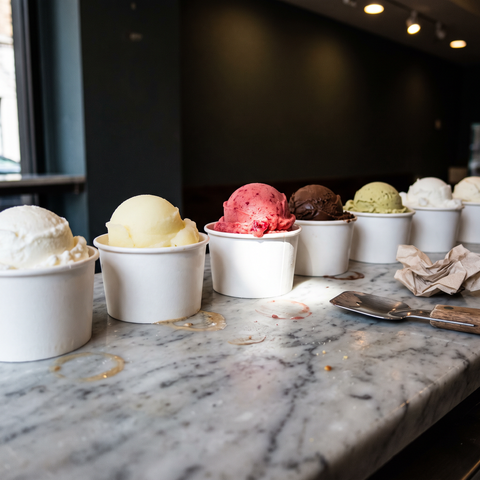 Coppette di gelato e sorbetto di gusti diversi allineate sul banco di marmo con una spatola
