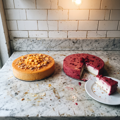 Due torte gelato affiancate su un piano di marmo, una ricoperta di glassa croccante al mango e una ai frutti rossi con una fetta tagliata nel piatto