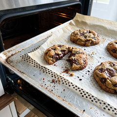 Biscotti con gocce di cioccolato appena sfornati su teglia forata con carta da forno e briciole