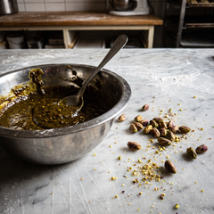 Pasta di pistacchio puro tostato in ciotola d'acciaio su marmo con pistacchi interi