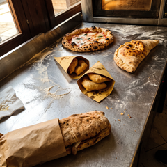 Pizza napoletana, calzone, pizze fritte e panuozzo dallo stesso impasto su banco da pizzeria